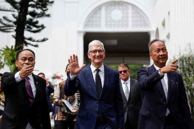 Tim Cook, center, smiling and waving, men on both sides of him are also waving