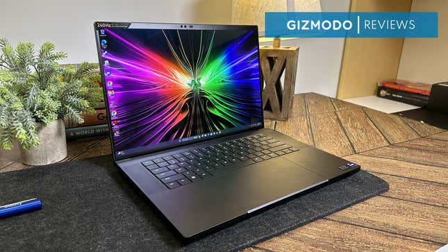A Razer Blade 16 gaming laptop on a table next to a plant and some books. 