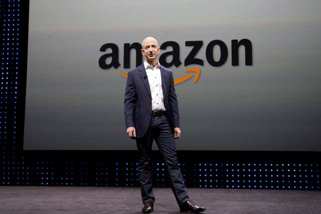 Jeff Bezos wearing a suit standing in front of a sign of the Amazon logo