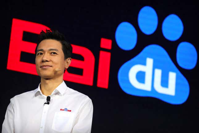 close up of Robin Li wearing a microphone and white button down ith Baidu Logo, the Baidu logo is displayed behind him, the du in the word is in a blue dog foot print