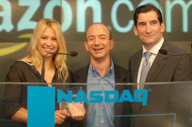 Anna Kournikova (left), Jeff Bezos (center), and Bob Greifield (right) stand closely together behind a clear podium that says NASDAQ