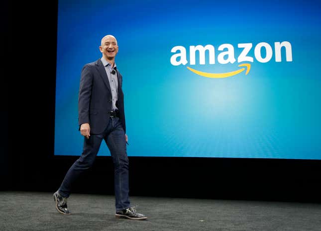 Jeff Bezos walks on stage, a blue backdrop with the Amazon logo is behind him