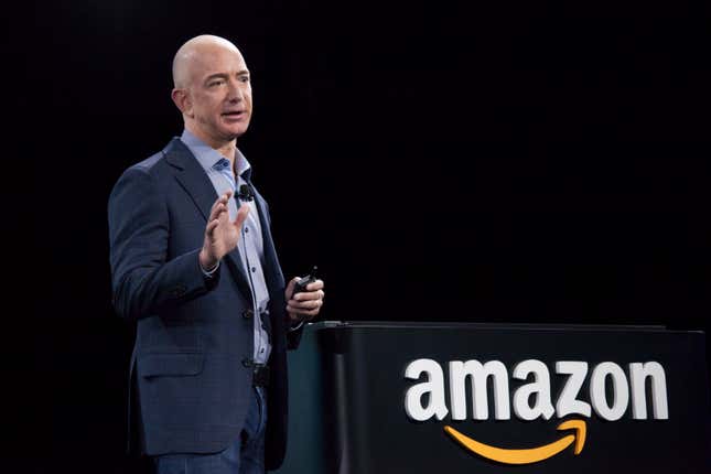 Amazon speaking with his hand up behind an Amazon sign