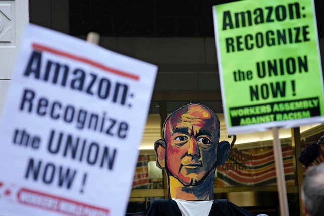 two activist signs that say "Amazon: Recognize the union now!" a painting of Jeff Bezos is between the signs